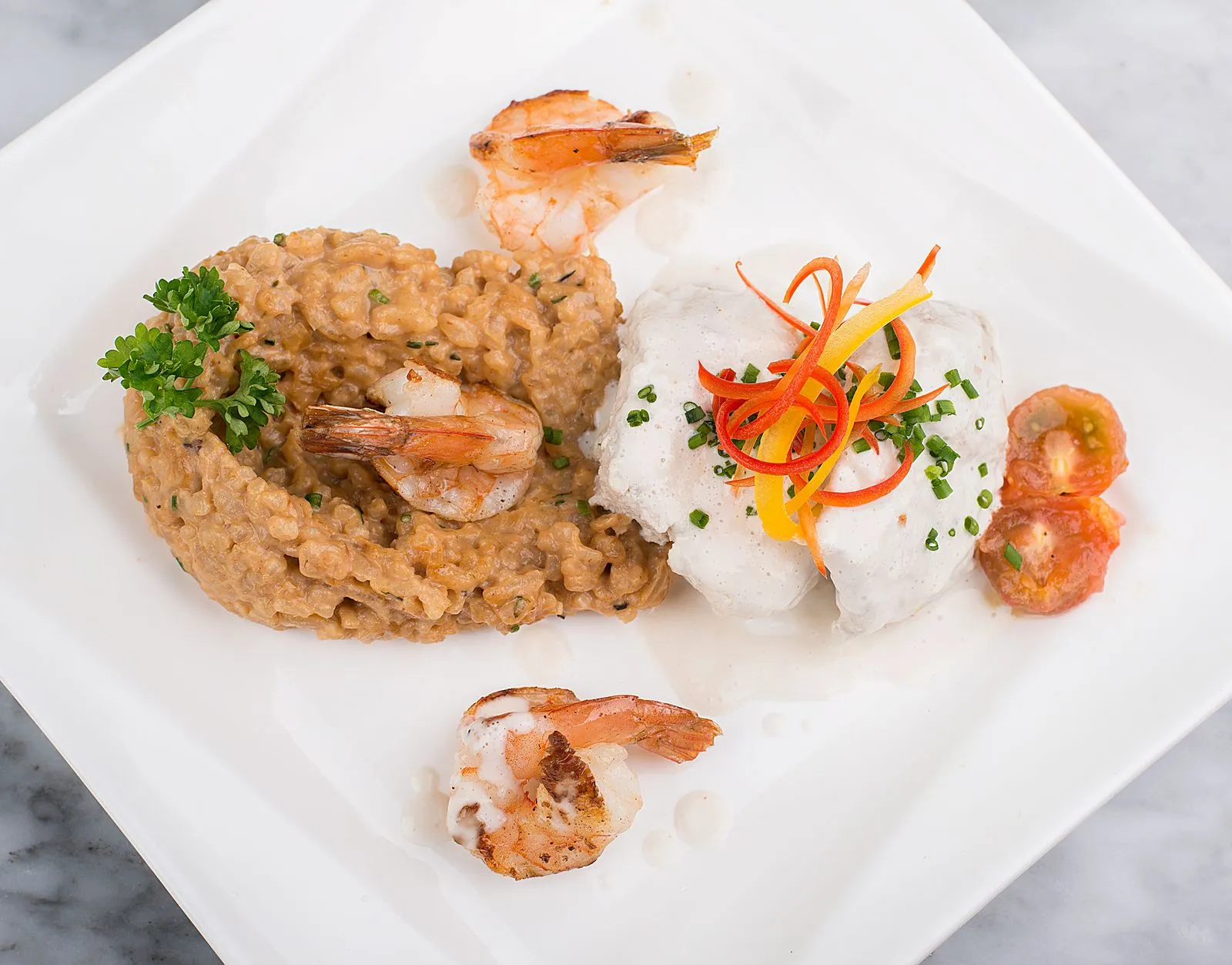 A top view of seafood risotto with shrimps, vegetables, and garnishes served elegantly on a square plate.